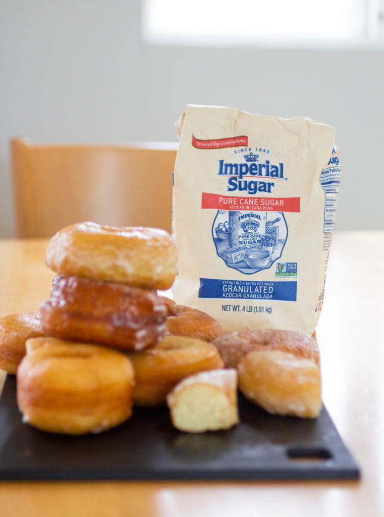 A bag of Imperial Sugar next to a tower of doughnuts.