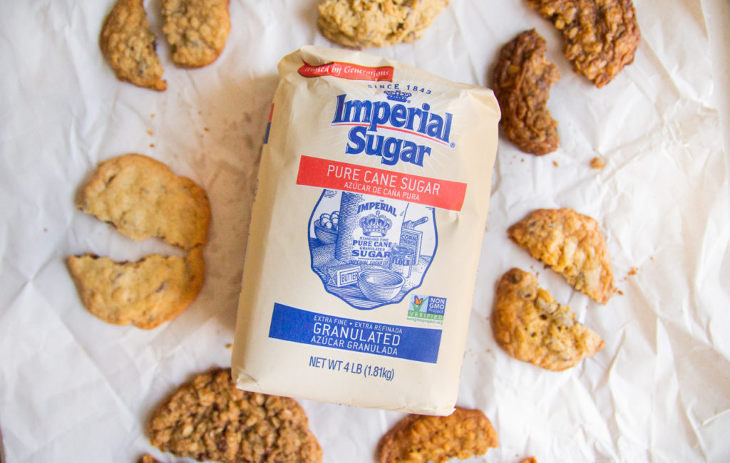 A bag of Imperial Sugar surrounded by half eaten oatmeal chocolate chip cookies.