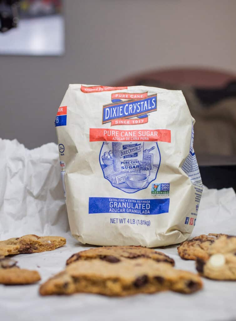 A bag of Dixie Crystals next to half eaten chocolate chip cookies.