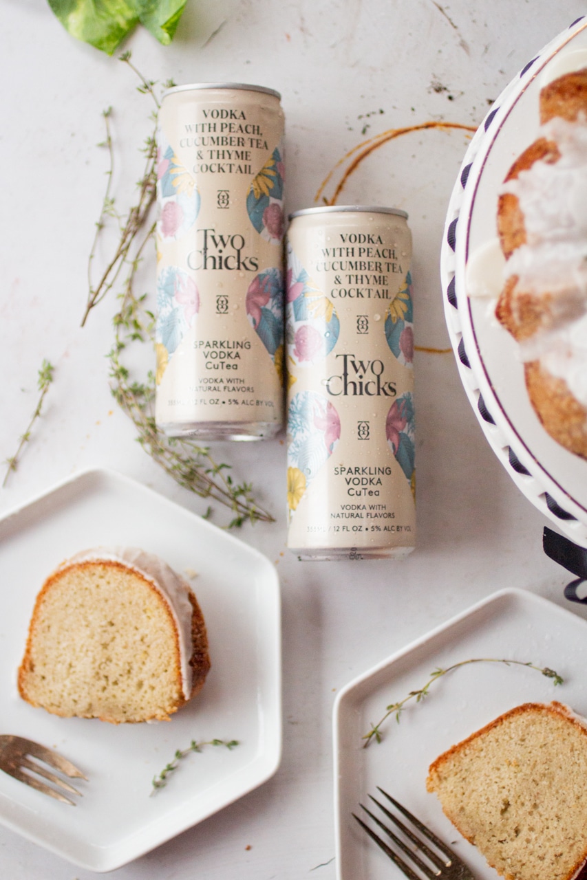 Two cans of Two Chicks next to slices of a frosted bundt cake on white plates.