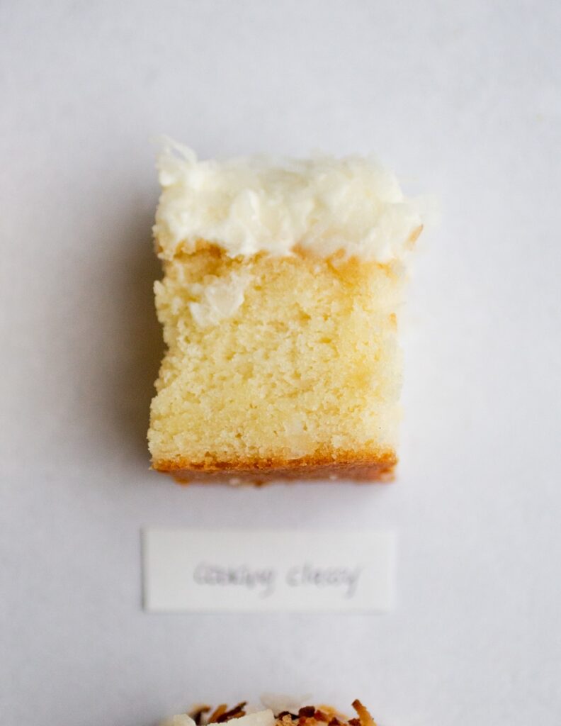 square of frosted coconut cake on a gray background with the label \"cooking classy.\"