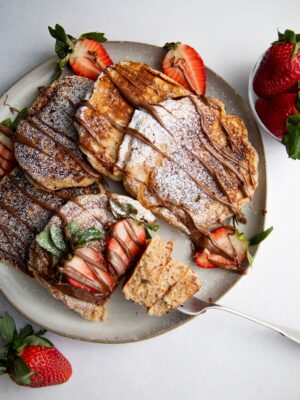 a plate of pancakes drizzled with nutella and strawberries.
