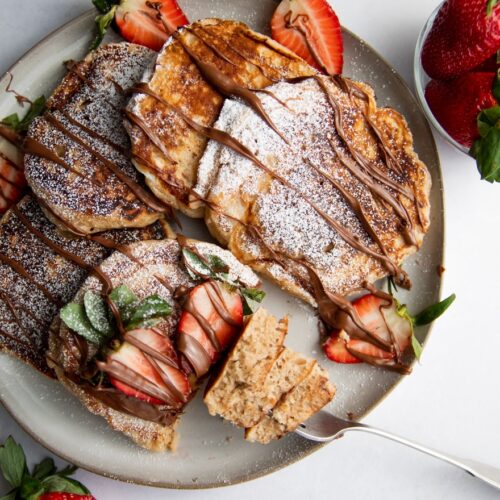 a plate of pancakes drizzled with nutella and strawberries.