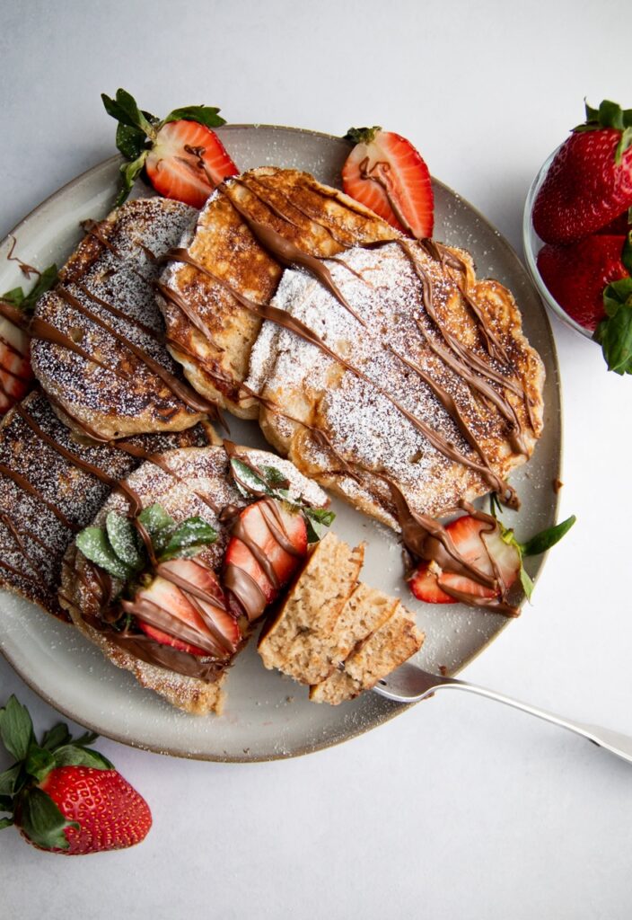 a plate of pancakes drizzled with nutella and strawberries.