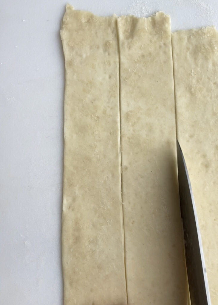 A sheet of rolled out puff pastry cut into long strips.