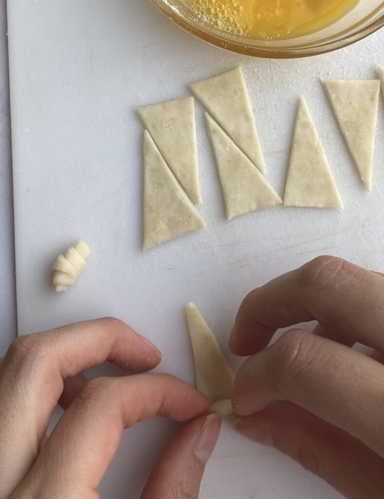 Rolling up a triangle of puff pastry into a mini croissant.