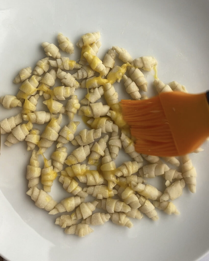 A bunch of tiny puff pastry croissants brushed with egg wash.