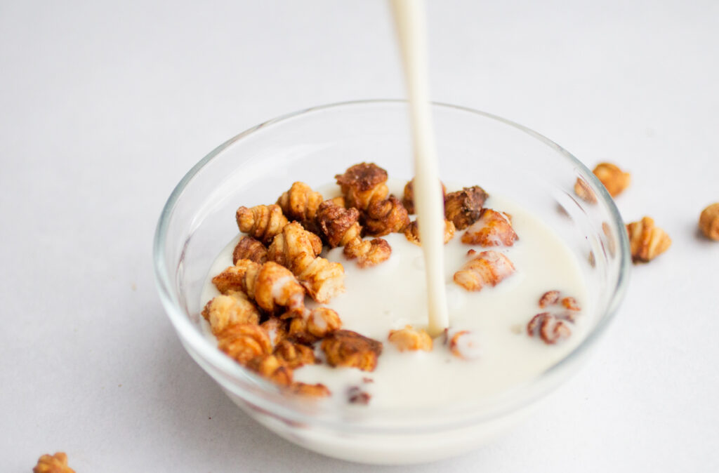 A glass bowl of mini croissant cereal with milk pouring into the bowl. 