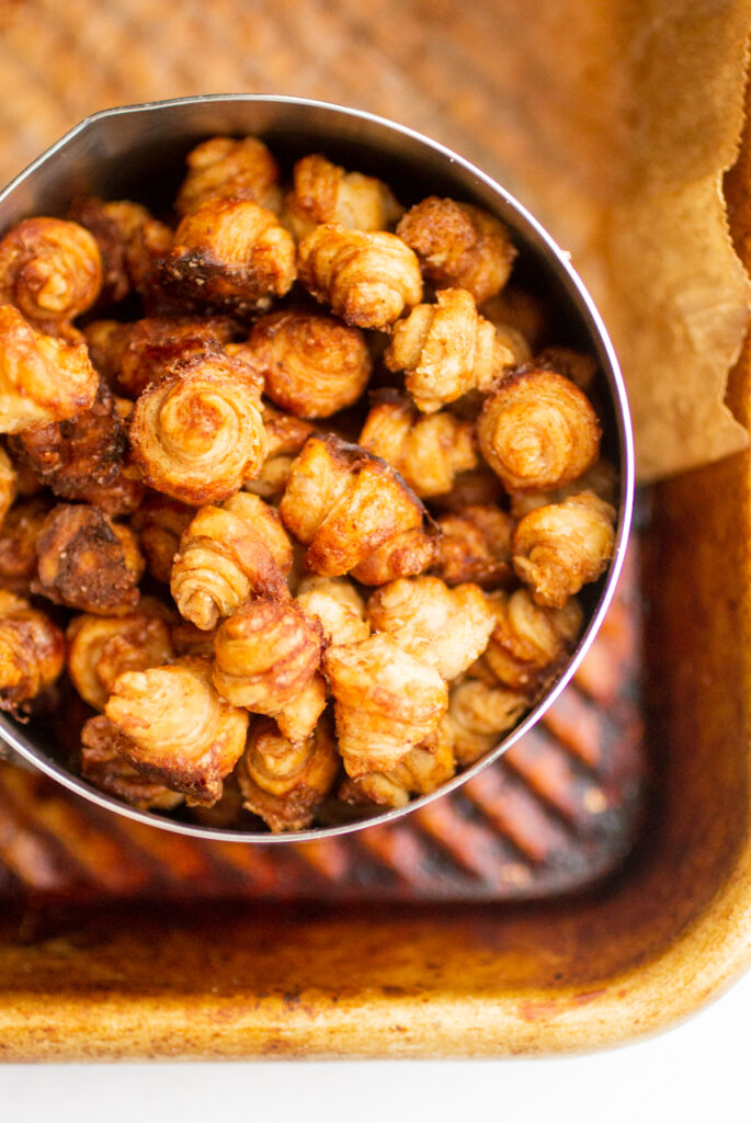 A measuring cup full of tiny croissant cereal.