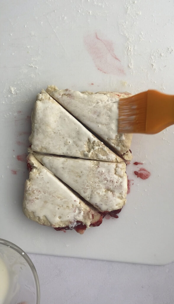 Brushing the cut scones with heavy cream.