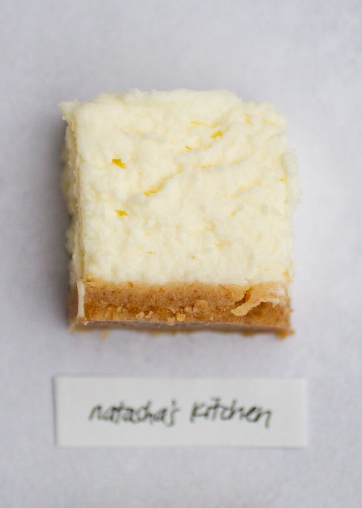 a square of natasha\'s kitchen\'s no-bake cheesecake on a gray background.