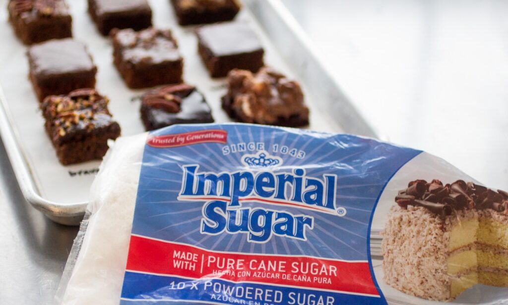 bag of imperial sugar in front of a tray of texas sheet cake squares.