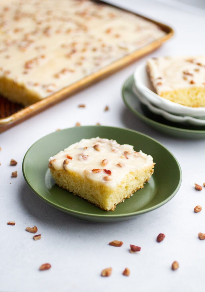 A slice of Texas sheet cake on a green plate with pecans sprinkled around.