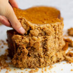 a hand picking up a slice of pumpkin bread on a white background.