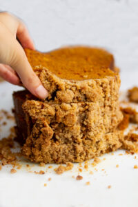 a hand picking up a slice of pumpkin bread on a white background.