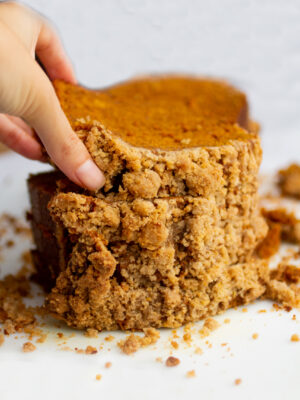 a hand picking up a slice of pumpkin bread on a white background.