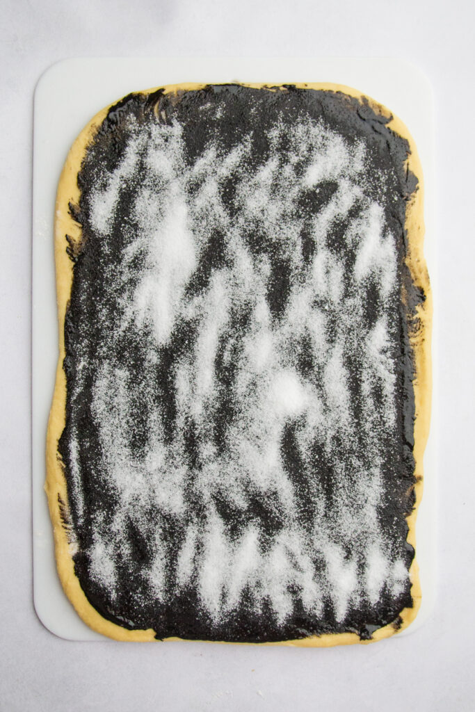 Rolled out dough with black sesame paste spread on top with sugar sprinkled over the top.