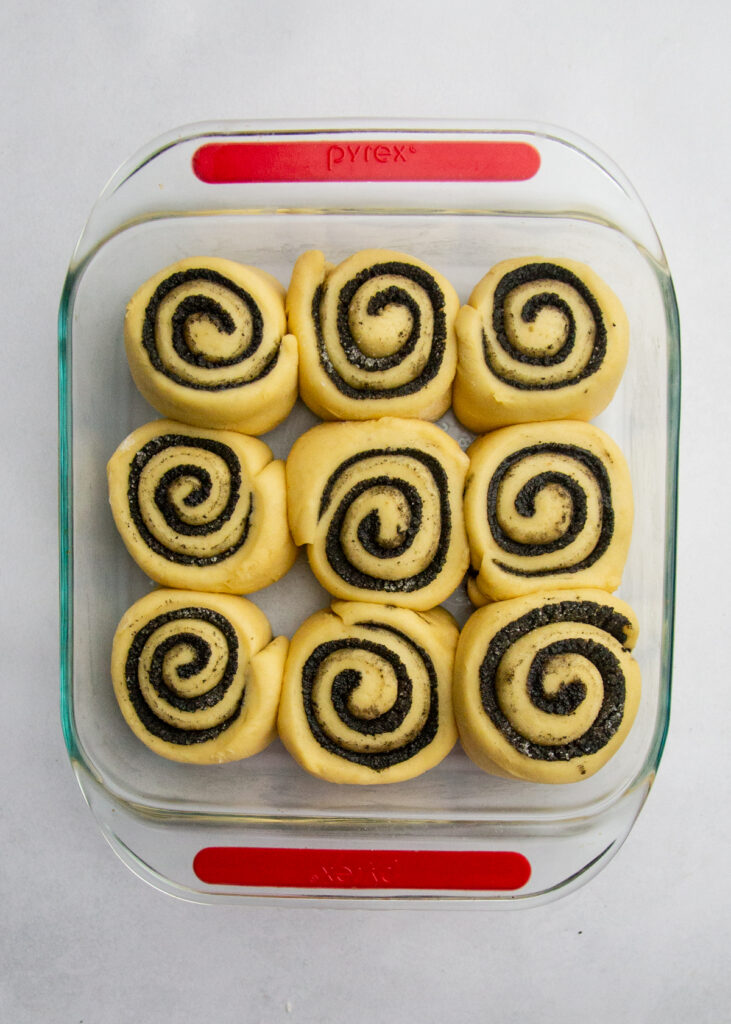 9 black sesame sweet rolls risen and puffy in a square baking pan.