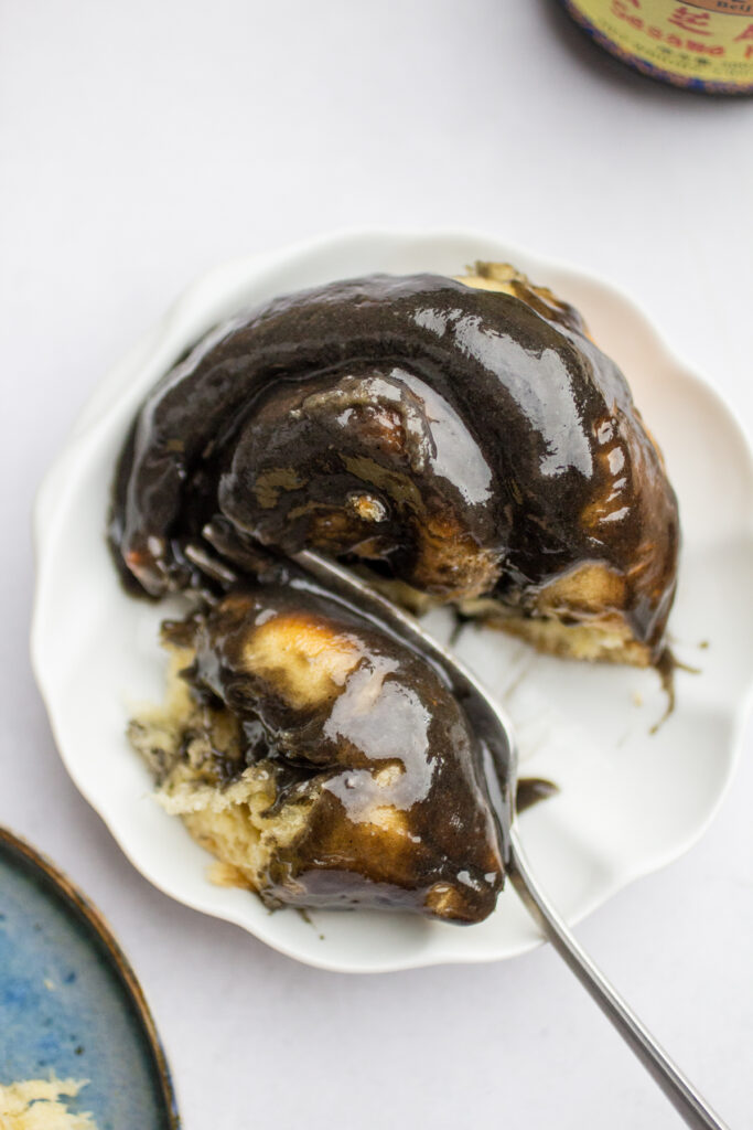 a fork taking a bite out of a glazed black sesame roll.