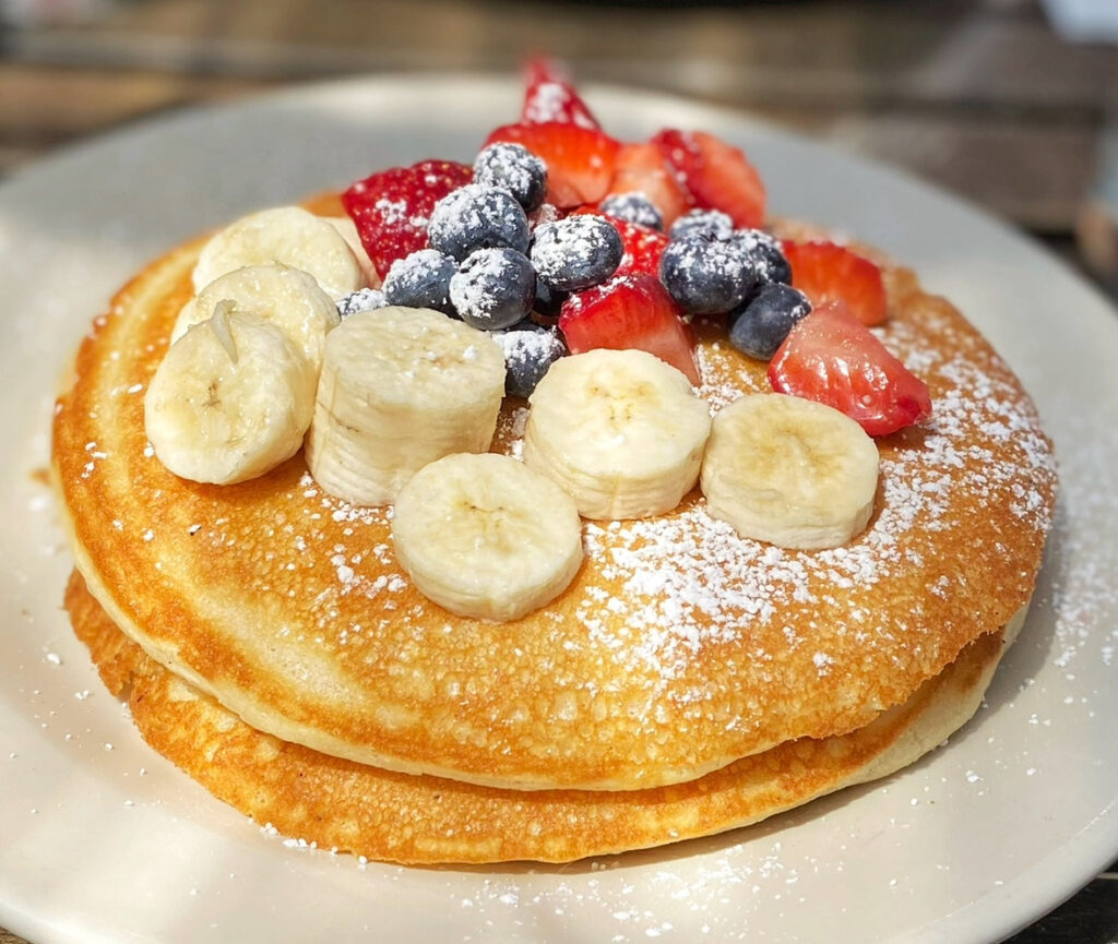 a double stack of pancakes with bananas and berries on a white plate.