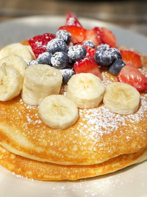 a double stack of pancakes with bananas and berries on a white plate.