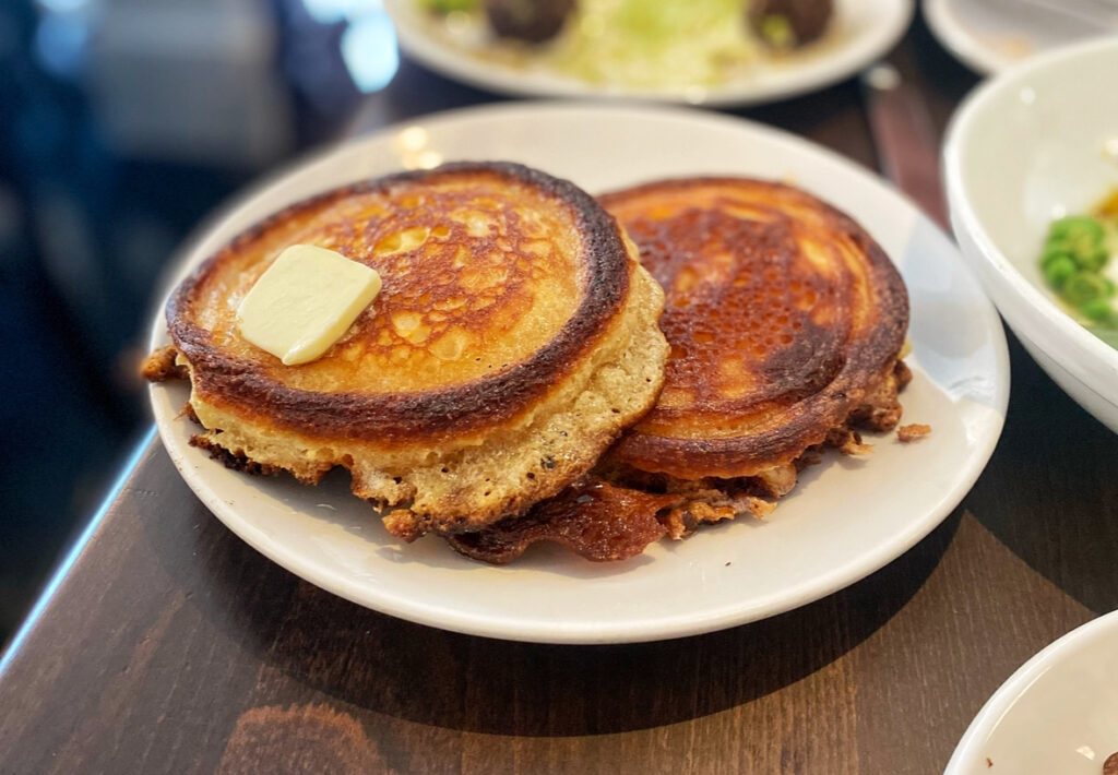 two crisp pancakes with a pat of butter on a white plate.