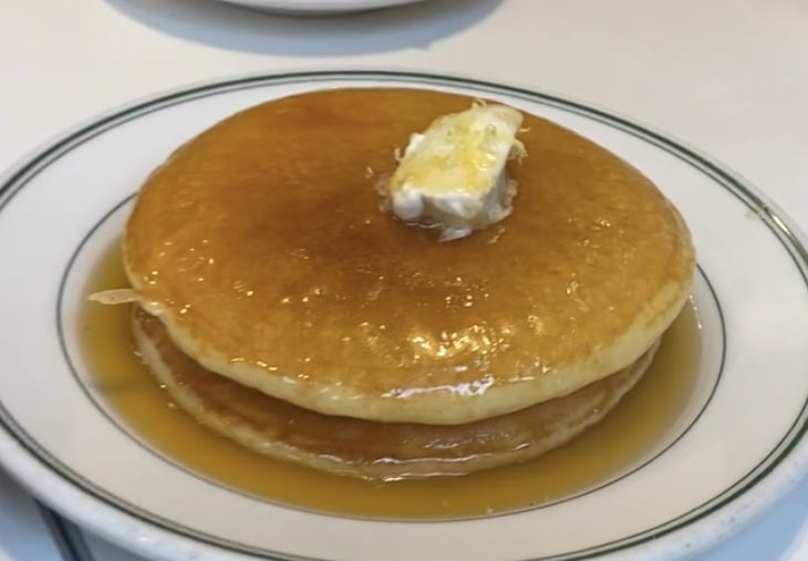 a stack of pancakes from Golden Diner with butter and syrup on a white plate.