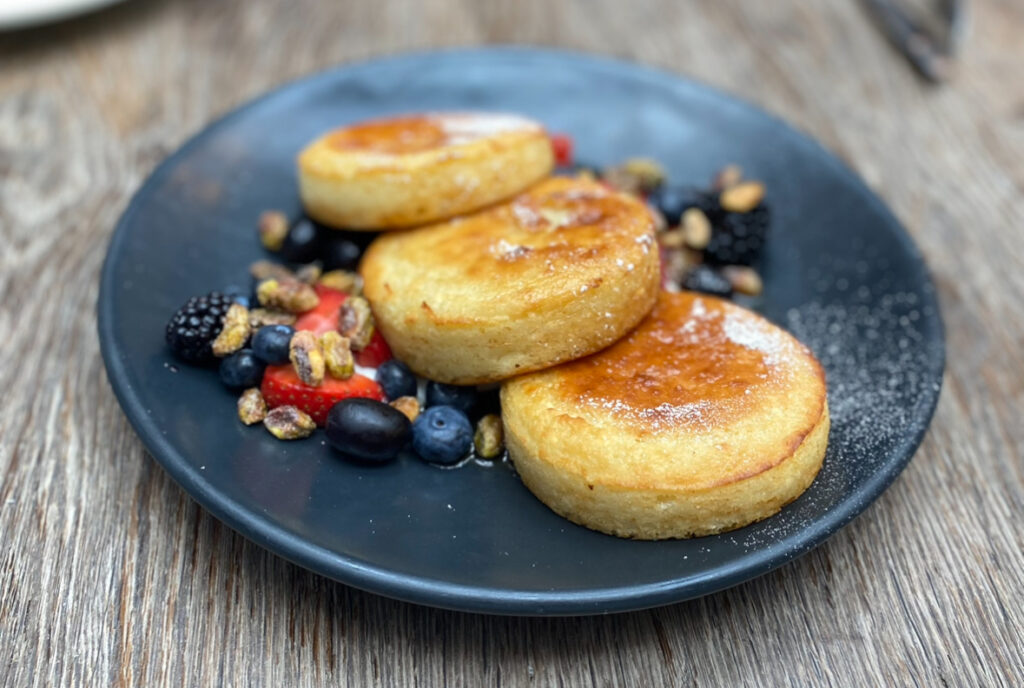 Three ricotta pancakes from Nomo Kitchen on a blue plate.