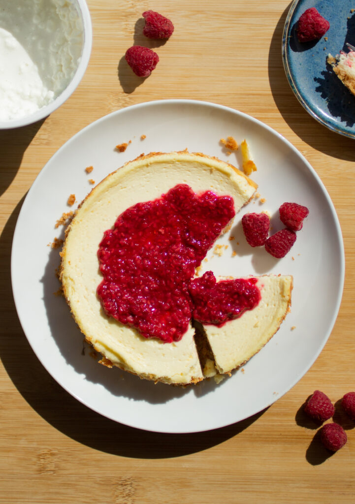 A cheesecake topped with a raspberry compote with a slice missing on a white plate.