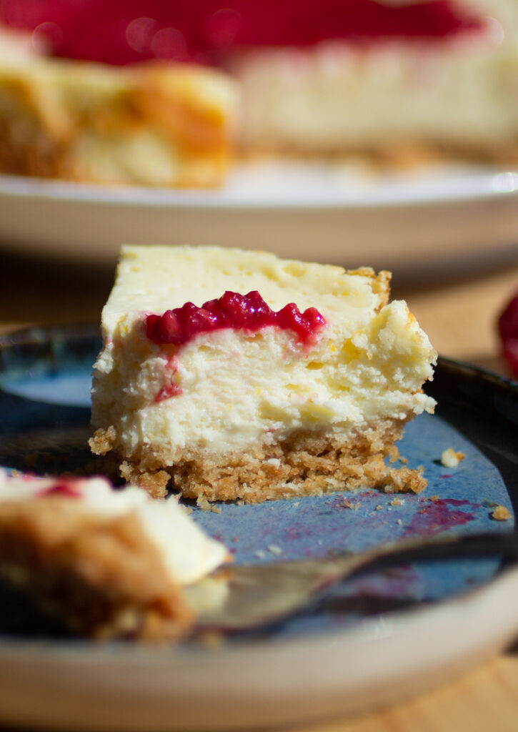 A close up on a bite taken out of a cottage cheese cheesecake topped with a raspberry compote.