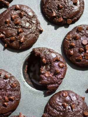 A half-eaten chocolate chip muffin in a mini muffin tin.