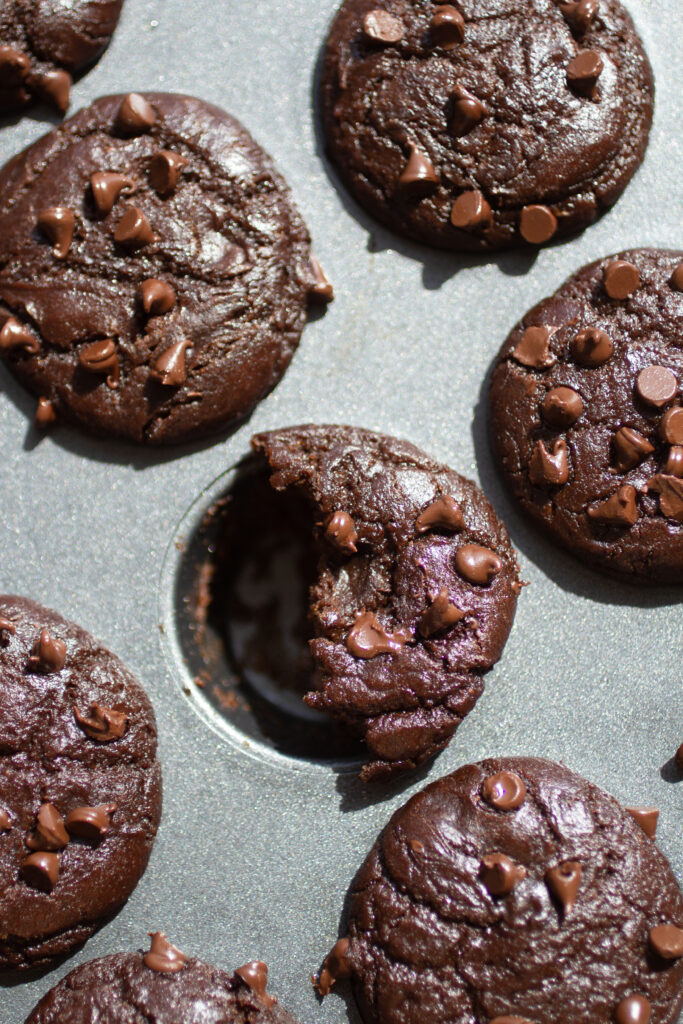 A half-eaten chocolate chip muffin in a mini muffin tin.