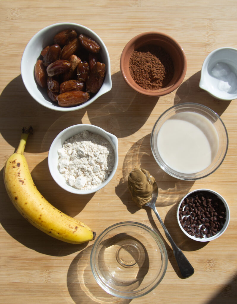 Ingredients for date-sweetened chocolate muffins: banana, dates, flour, cocoa, milk, oil, salt, mini chocolate chips.