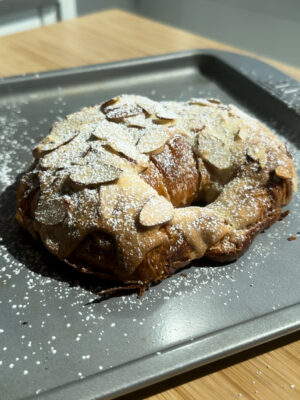 An almond croissant with powdered sugar on a gray baking pan.