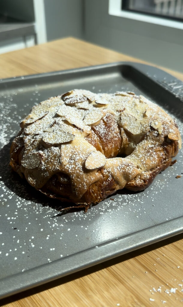 An almond croissant with powdered sugar on a gray baking pan. 