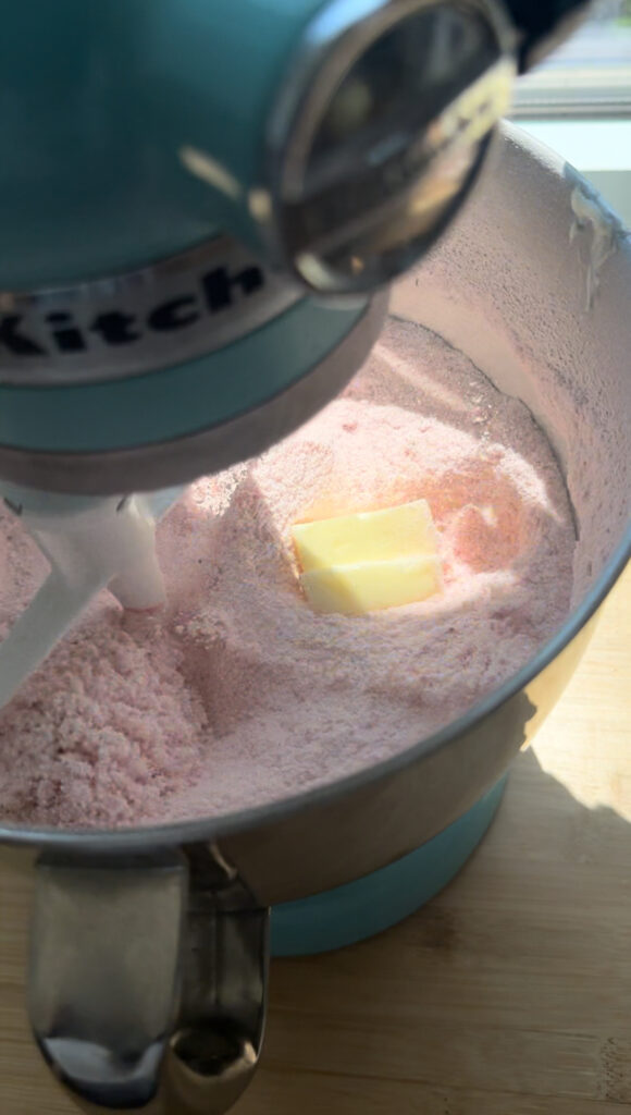 A mixing bowl with powdered sugar, freeze-dried strawberries and a pat of butter.