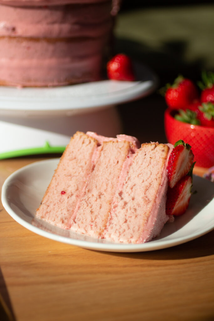 a slice of triple layer strawberry cake on a white plate.