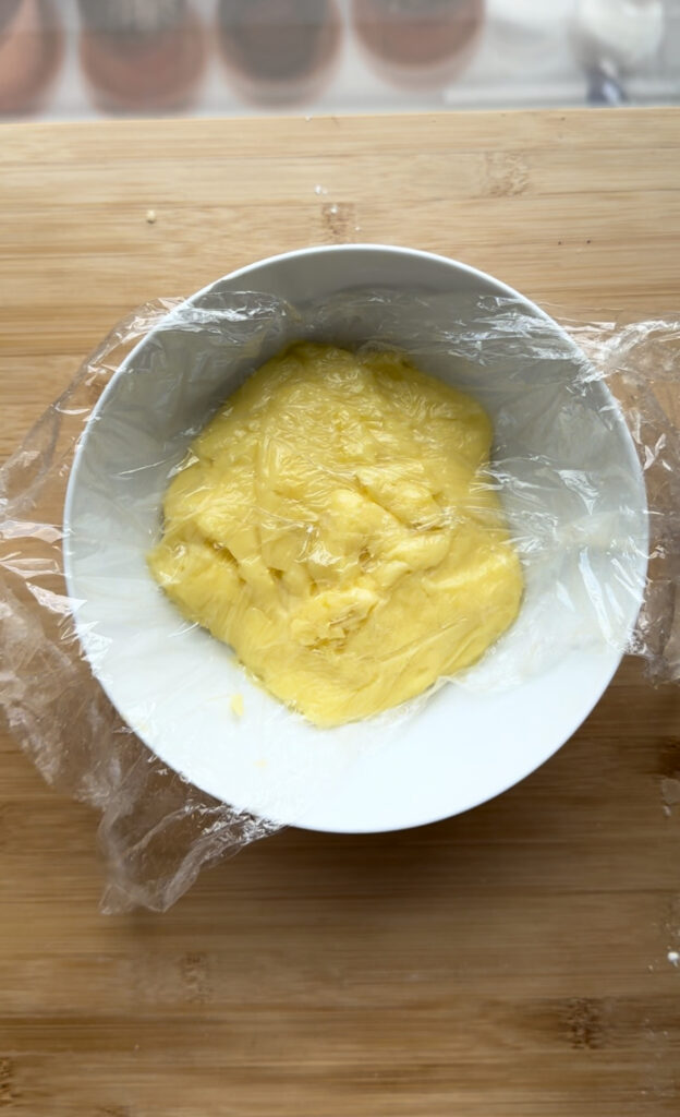 Custard in a white bowl covered with a plastic wrap.
