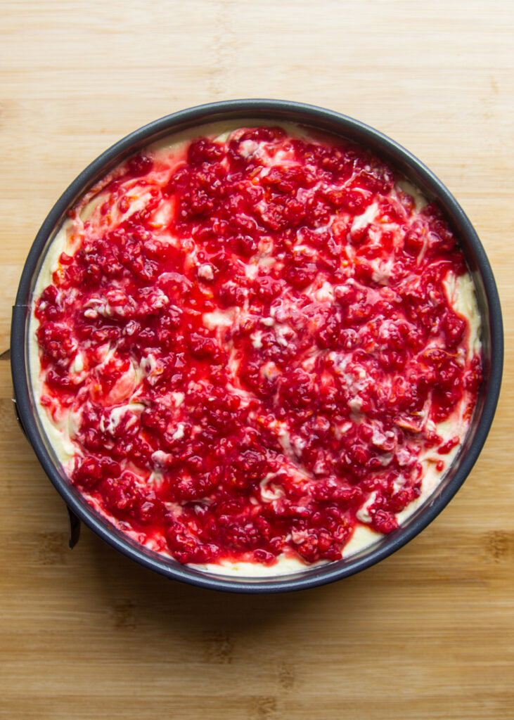 Macerated raspberries layered over mascarpone cream in a round pan.