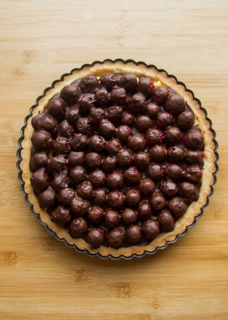A baked tart shell filled with raspberries, covered in a layer of chocolate.