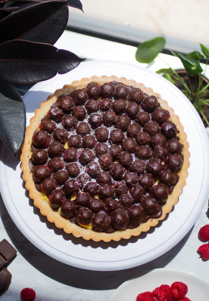 A whole raspberry chocolate tart on a white platter.