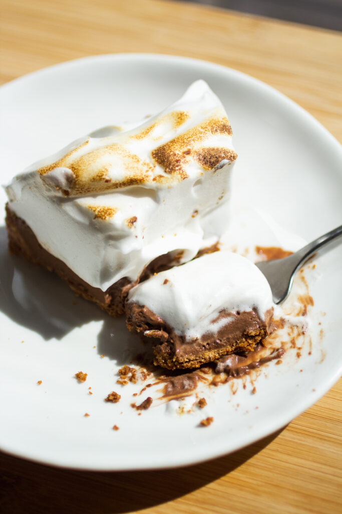 Bite taken out of a chocolate s\'mores pie on a white plate.