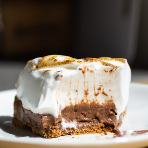 a half eaten slice of chocolate s'mores pie on a white plate.