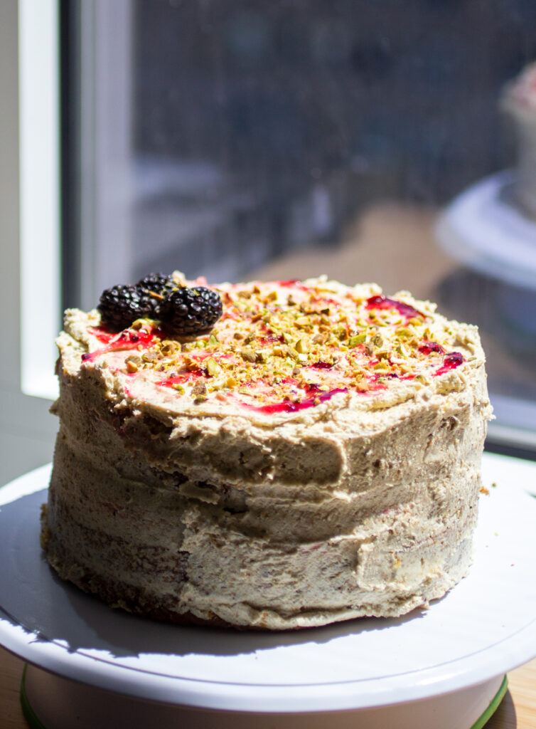 an olive oil cake on a cake stand with pistachio buttercream topped with blackberries.