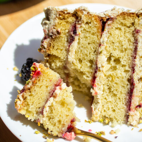 a slice of a four layer olive oil cake on a plate with a fork cutting a bite.