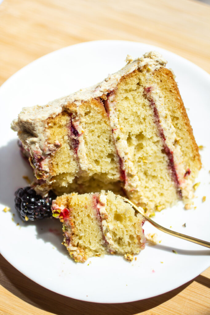 a slice of a four layer olive oil cake on a plate with a fork cutting a bite.