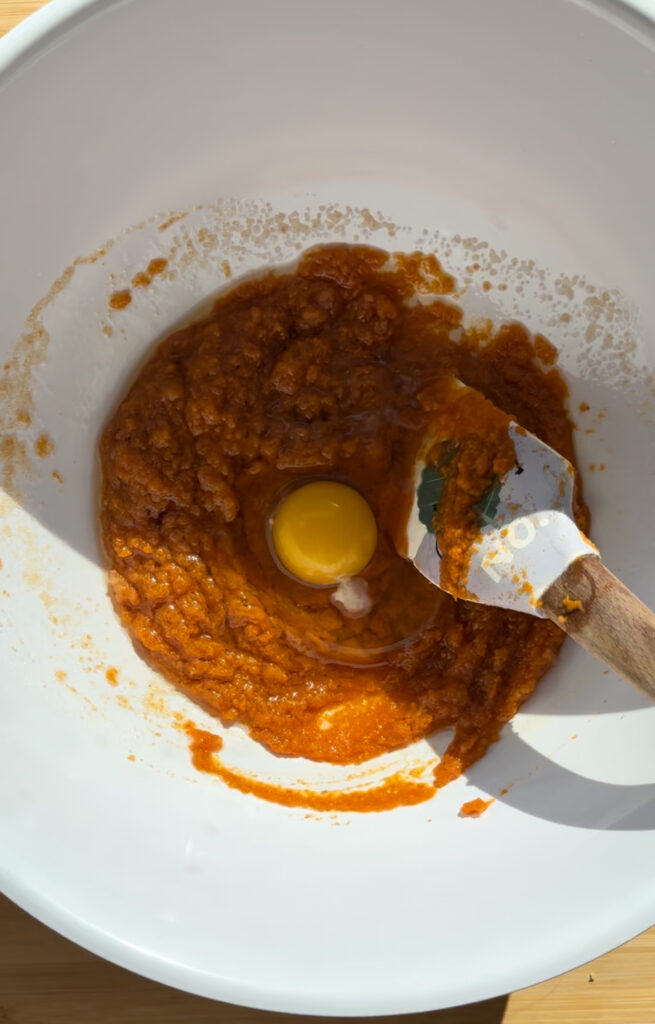Pumpkin puree and an egg in a white bowl with a spatula.