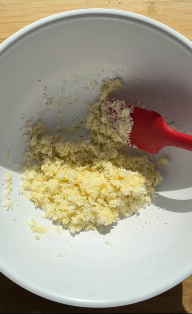 Grated cheese mixed with butter in a white bowl.
