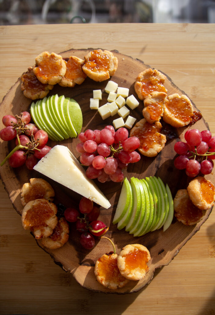 Overheat shot of a cheeseboard with grapes, apples, cheese and Pecorino Romano thumbprint cookies.