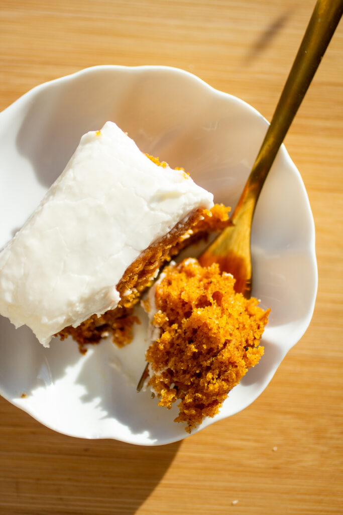 A bite taken out of a square of pumpkin sheet cake with a gold fork.